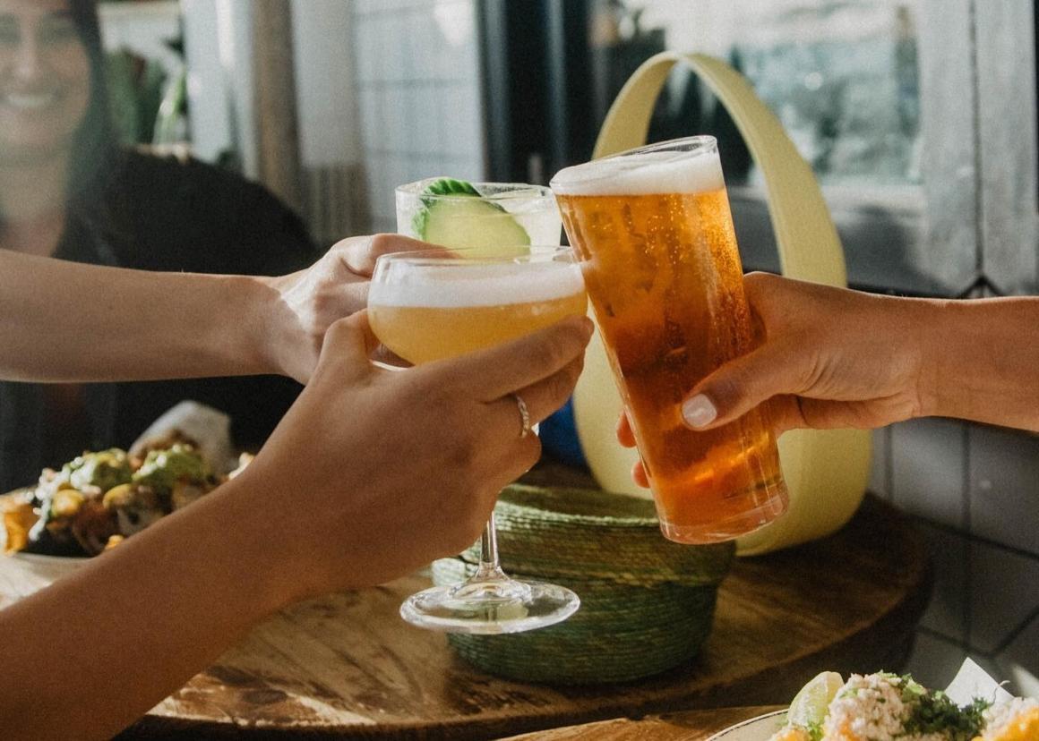 Three people cheers beers and cocktails over a table at Mexican bar El Grotto in Scarborough
