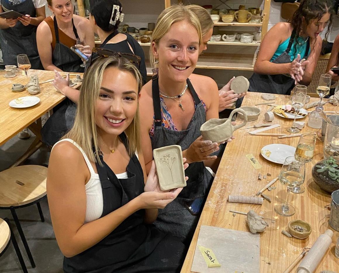 Two girls hold up their pottery at Perth Pottery Studio. One of Perth's best beginner pottery workshops