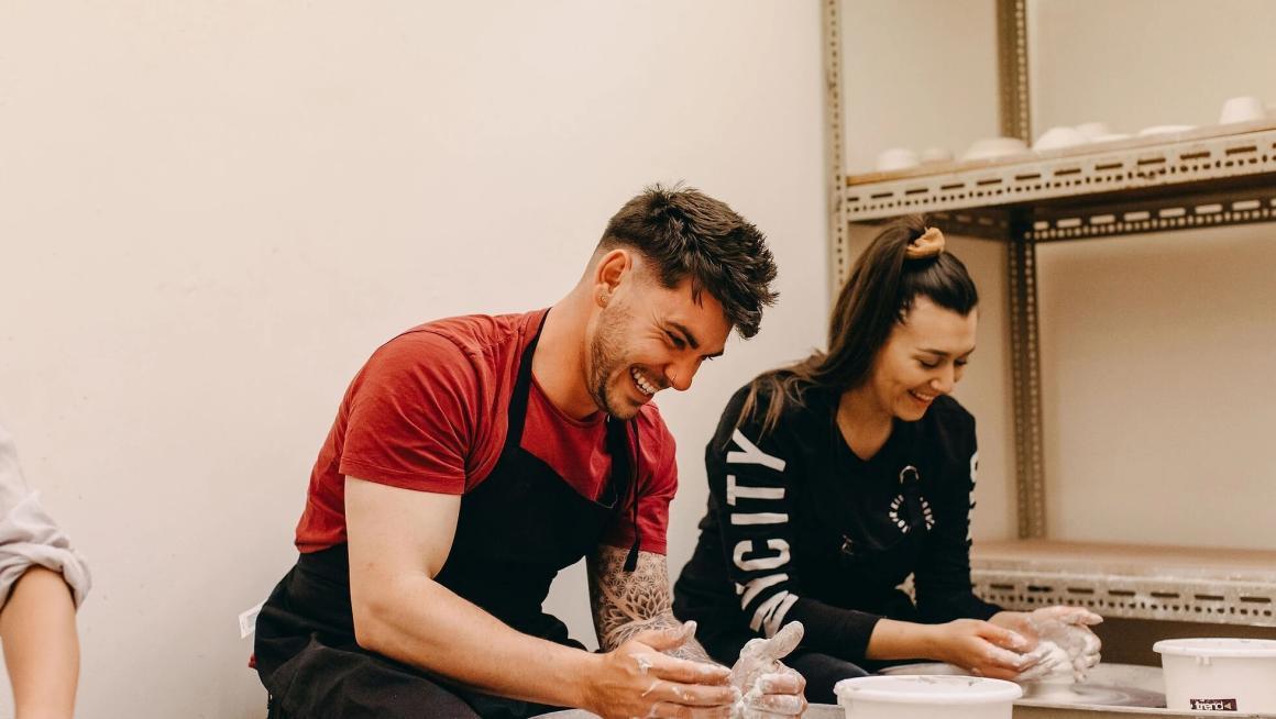 A couple making a cup on a wheel out of pottery at Not Yet Perfect. One of Perth's best beginner pottery workshops