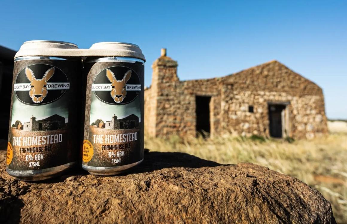 Two cans of the homestead lager by Lucky Bay Brewery sit on a rock in front of an old building