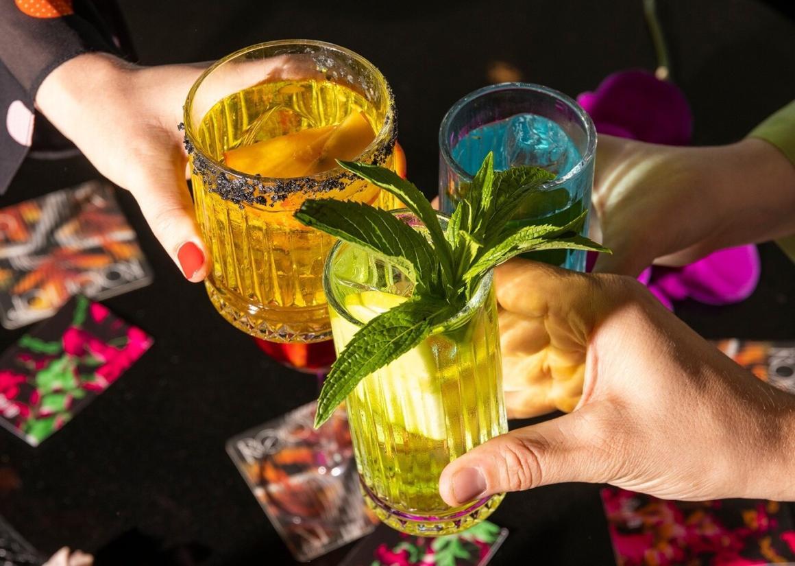 Three people cheersing colourful drinks at QT Rooftop bar. 