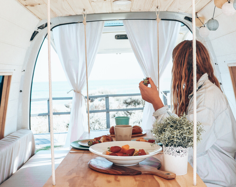 A woman sits in the INDI campervan eating at a hanging table. One of the best instaworthy campervans in WA