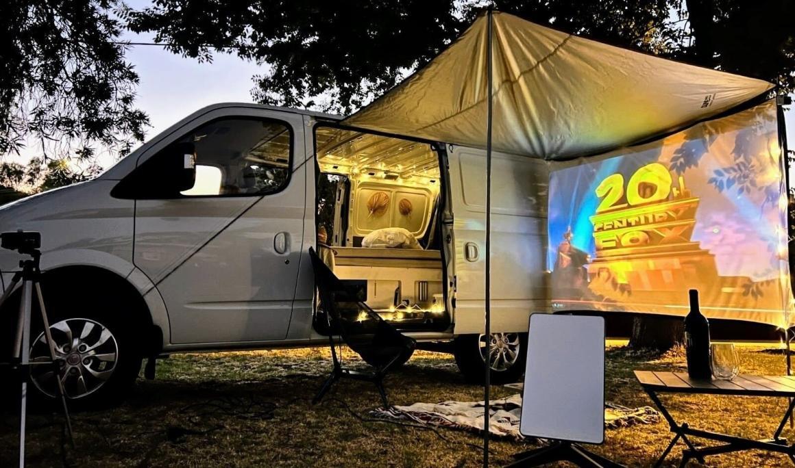 A wide shot of the outside of the OFF-GRID campervan with a movie projector set up. One of the most Instaworthy campervans