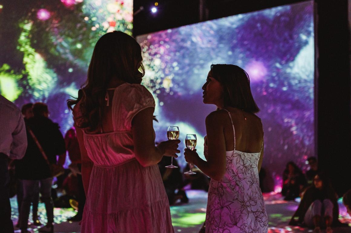 Two women chat whilst holding champagne and admiring the work in the Monet in Paris exhibit