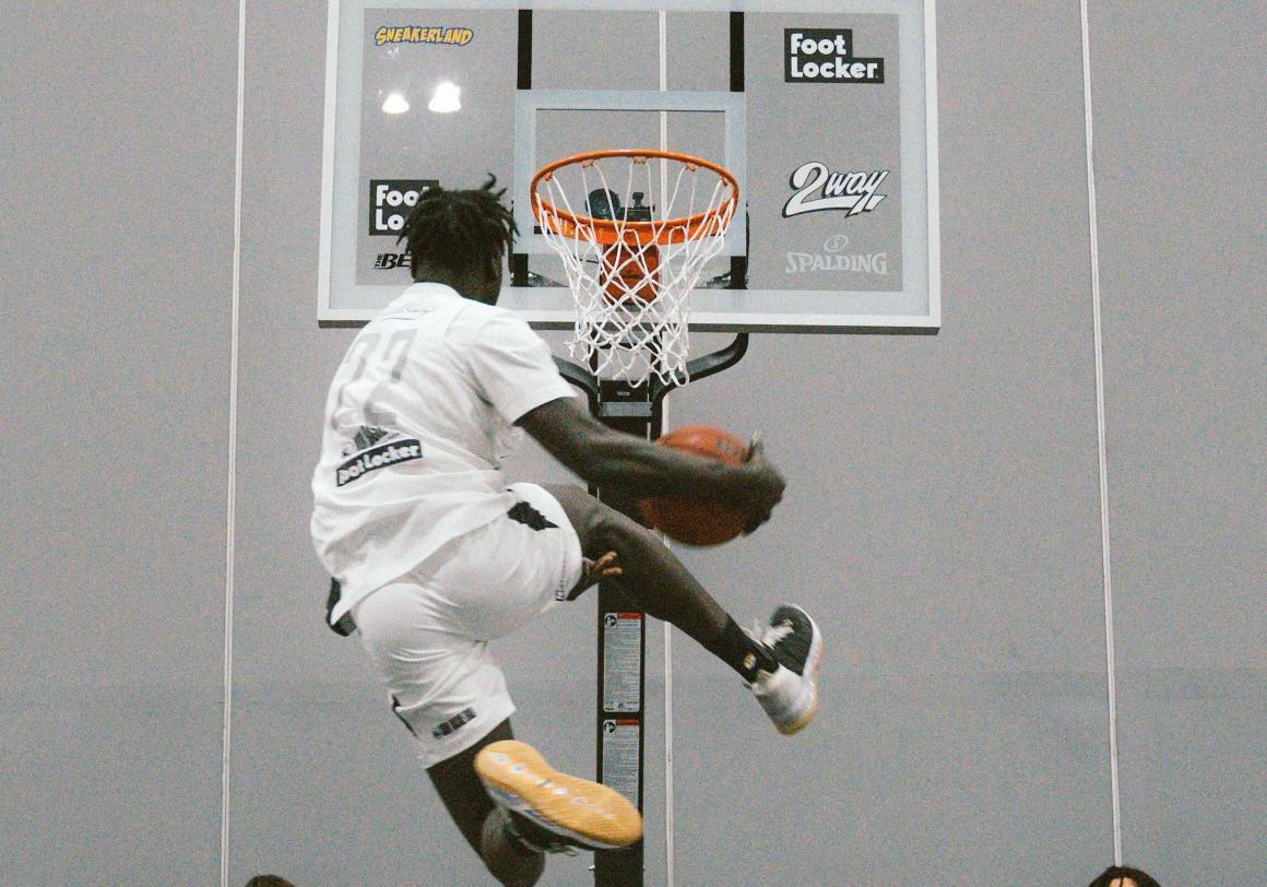 A basketball player jumping over another player to dunk a ball in a hoop at the Sneakerland convention in Perth