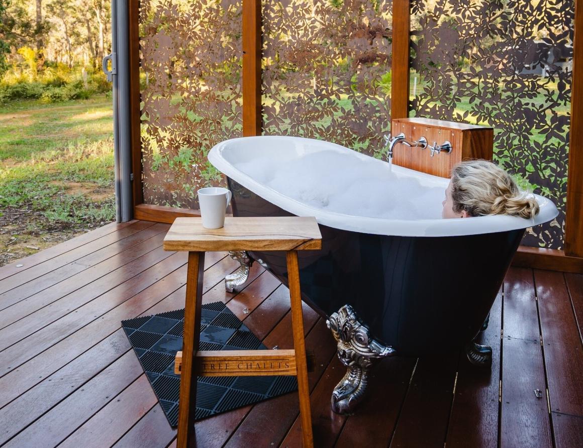 A woman soaks in an outdoor bath on the patio of the Tree Chalets. One of the best accomodations in Busselton to stay at