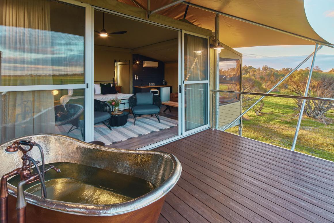 The patio view of Willow Wood Glamping Retreat, one of the top places to stay in Busselton. Shows the wooden deck, copper bath, bedroom view and Australian bush scenery