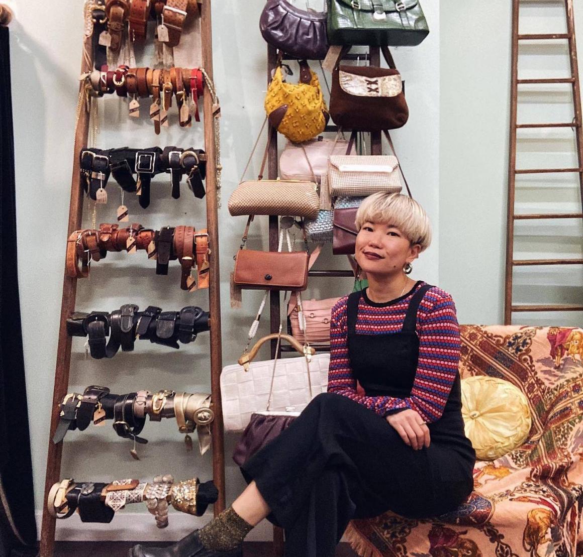 A photo of Fi from fi & co sitting in her store in front of vintage belts and bags. One of the best vintage clothing stores in Perth city