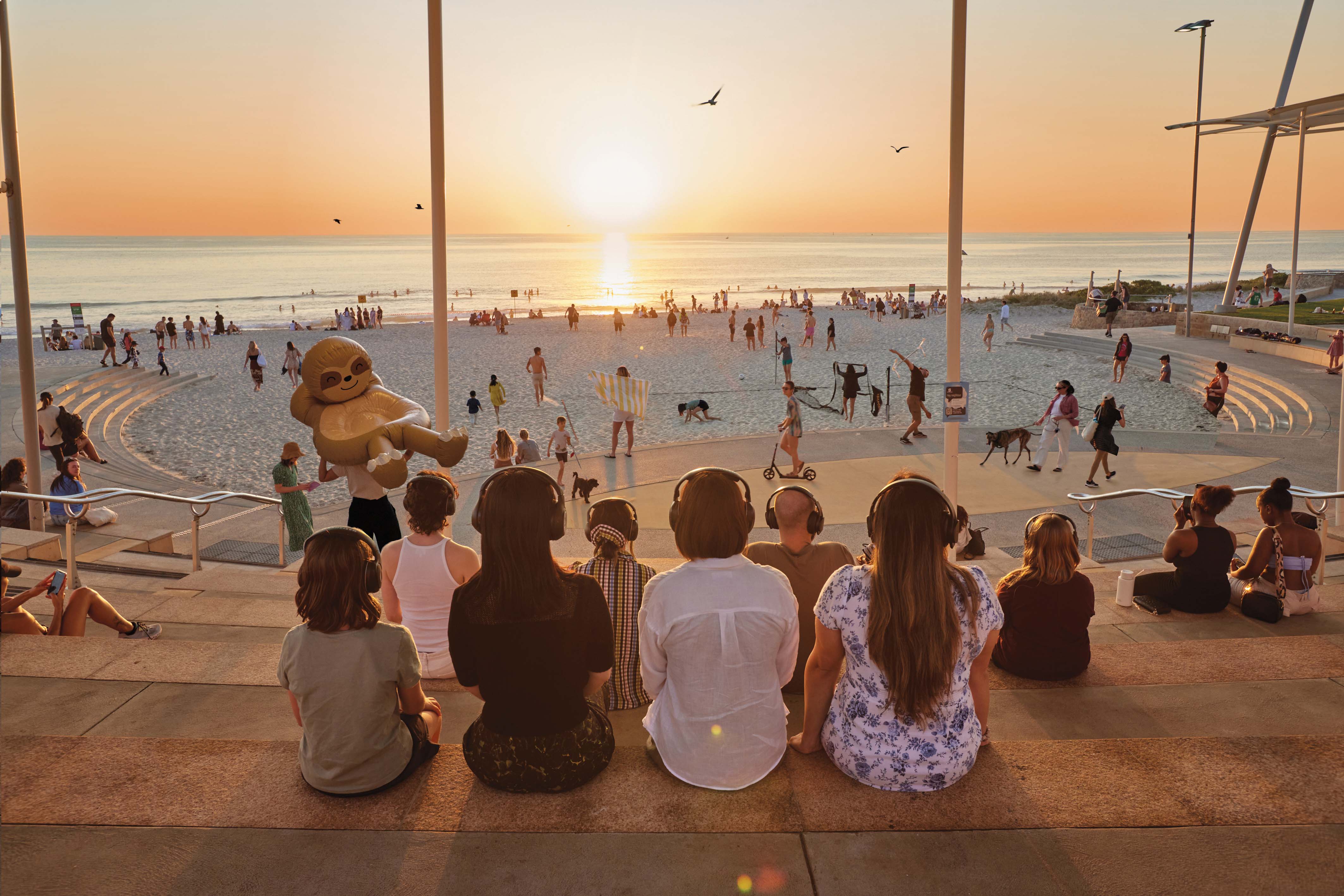 A group of people sit at the Scarborough Beach amphitheatre wearing headphones as they partake in the invisible opera