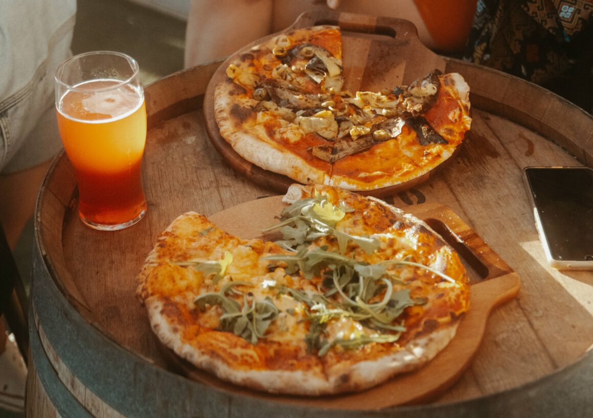 Two woodfired pizzas and a beer on one of Froth North Beaches wine barrel tables