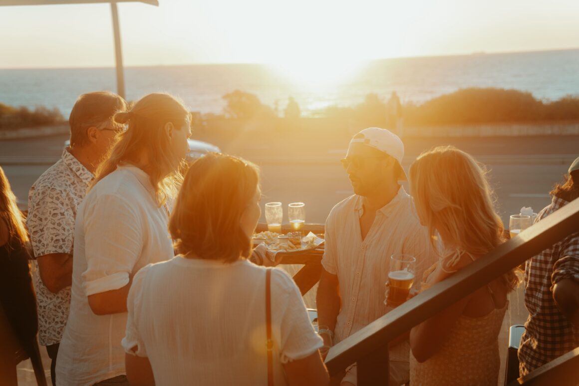A group of people enjoying drinks on the terrace at Froth North Beach with the sunsetting behind them