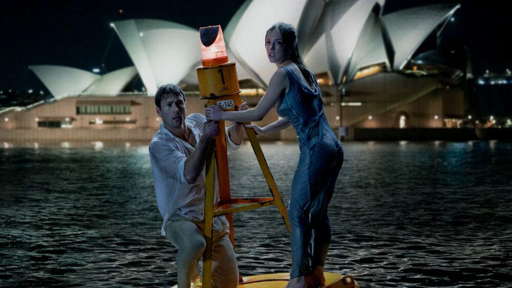 A still from Anyone But You with the two main characters in the water in front of the Sydney Opera House