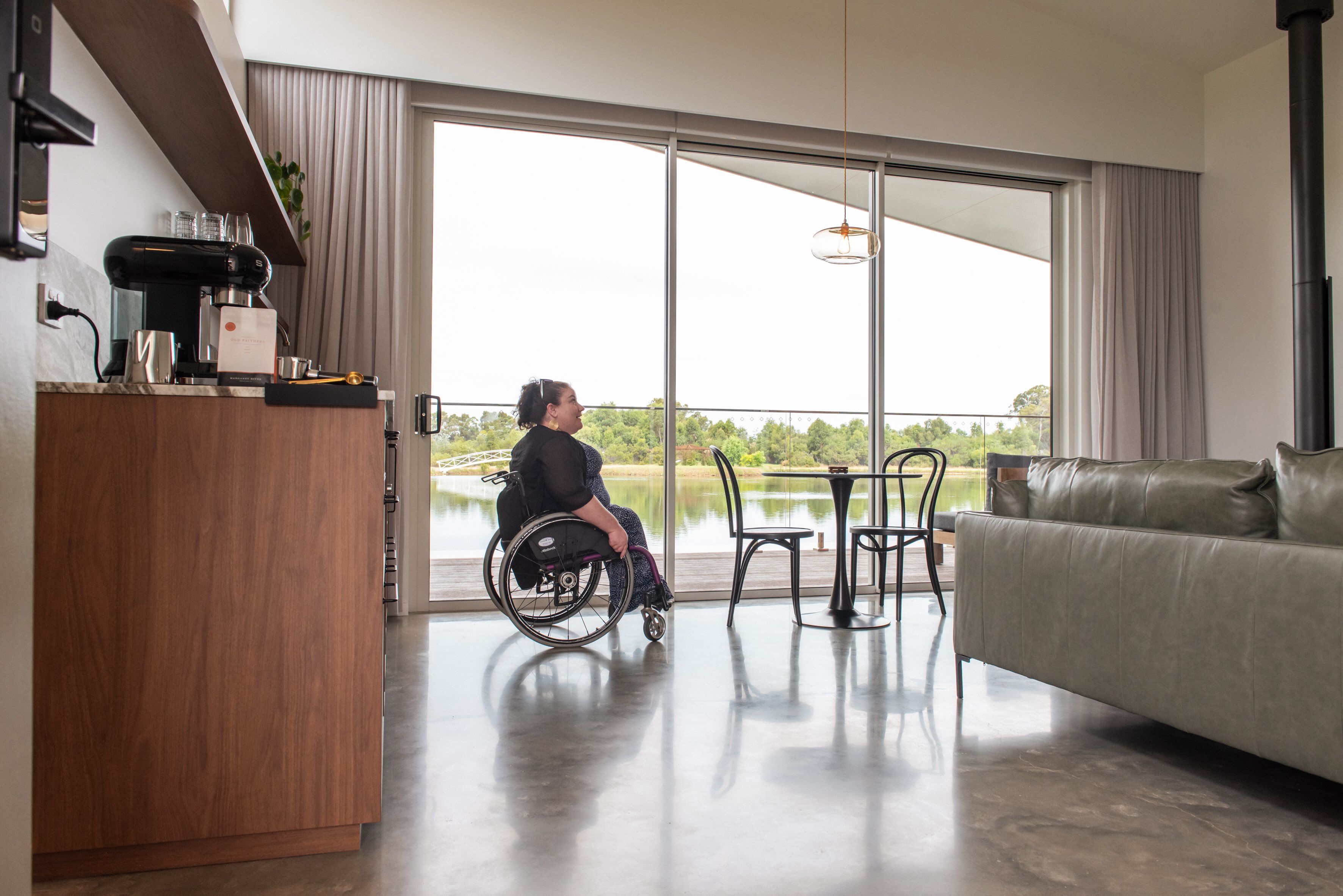 A woman in a wheelchair in the living room of villa 1 near the balcony door 