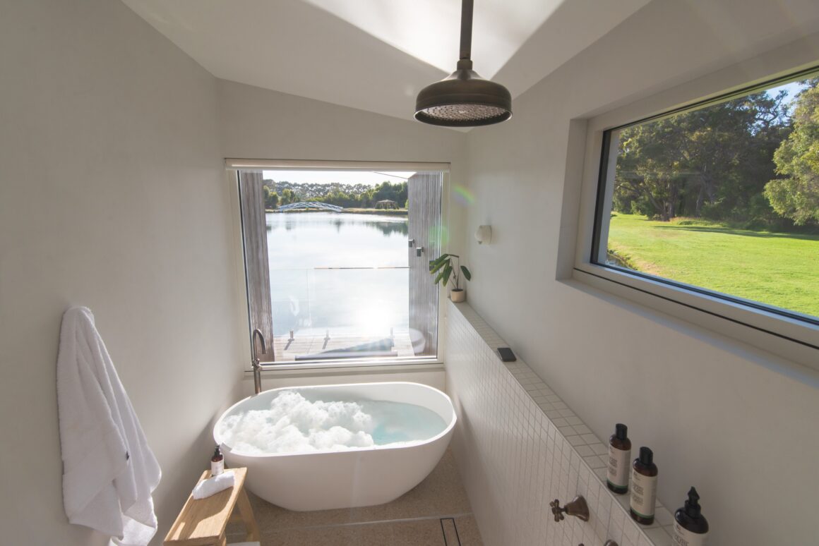 A photo of a villas bathroom showing the free standing bath tub up against the window showing the lake view