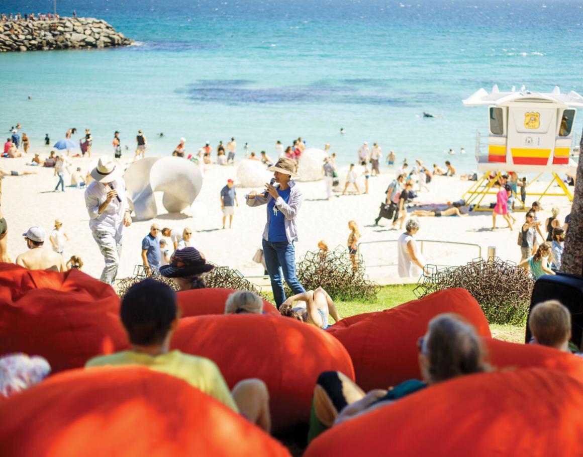 An artist talks about their work on the Cottesloe shoreline, whilst an audience of people sit on beanbags listening