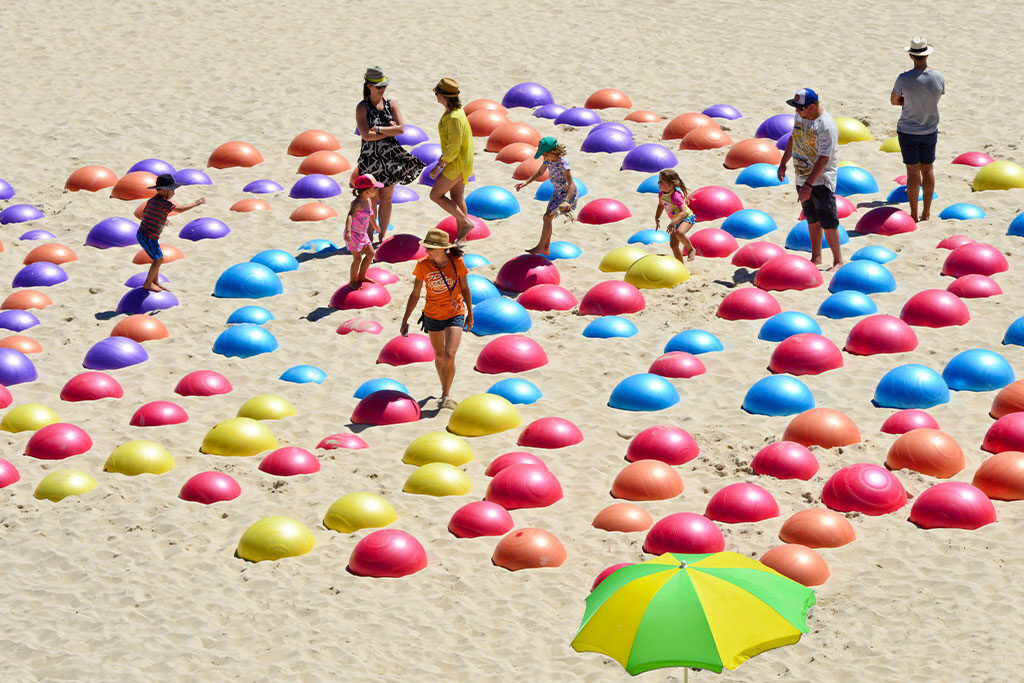 Children running across an art piece with colourful exercise balls buried in the sand