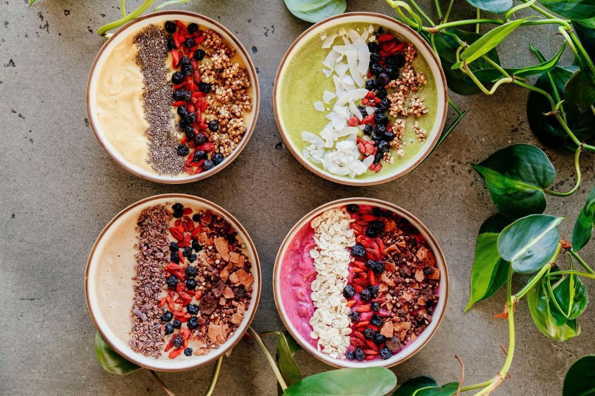 Four deliciously topped acai bowls sit on a table with greenery positioned around it in Pressed Earth's store.