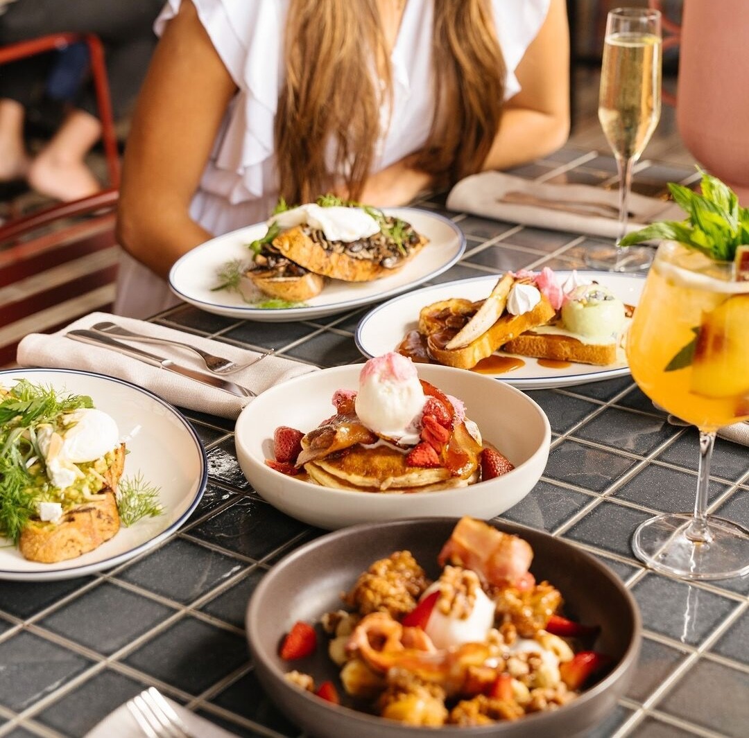 Several brunch food items sit on a grey tiled table with cocktails at The Claremont Hotel