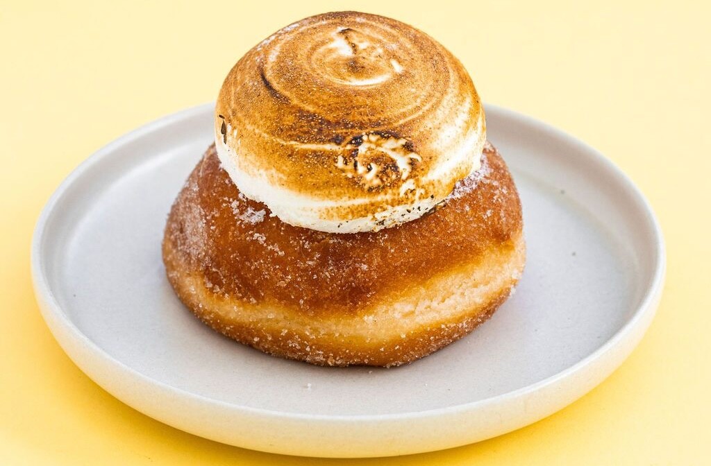 A lemon meringue donut sits on a plate on a yellow background at Crumbs Patisserie