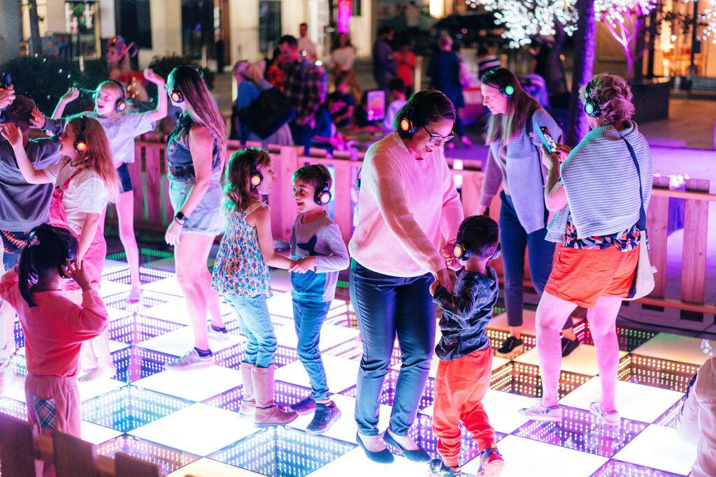 Parents and children enjoy a silent disco on a lit up dance floor