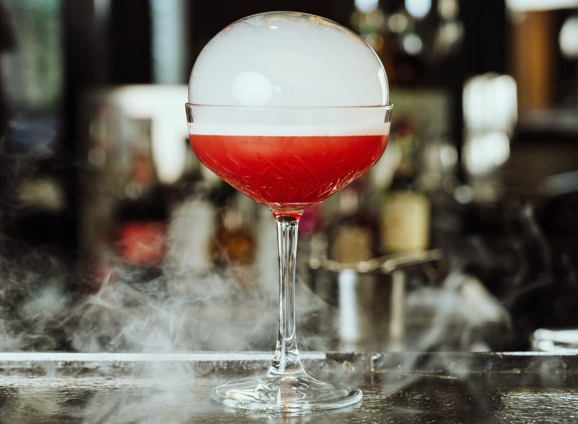 A red cocktail with a bubble of smoke sitting atop it