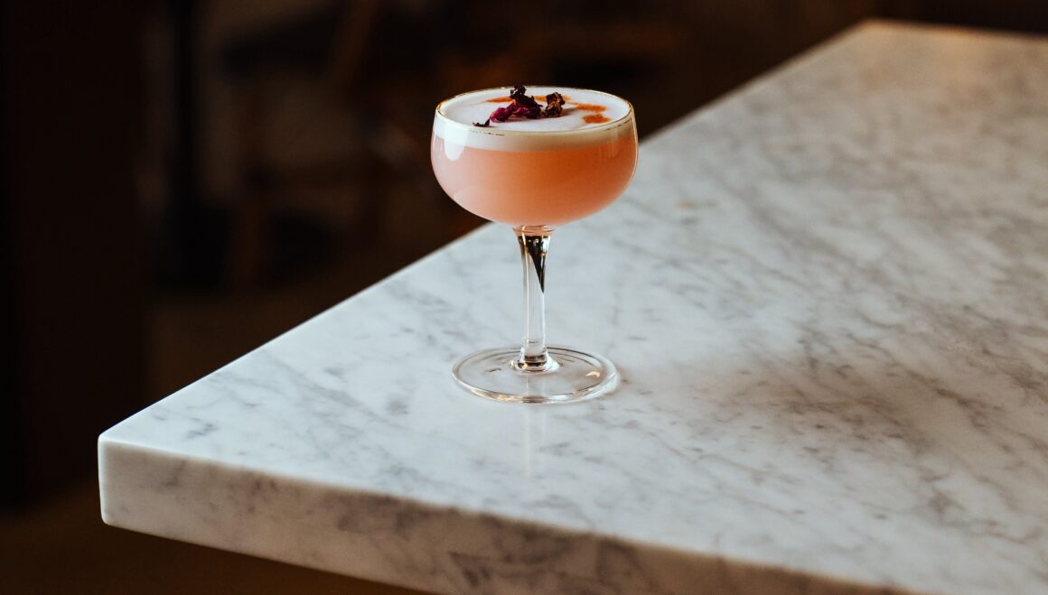 A pretty pink cocktail sits on a marble countertop 