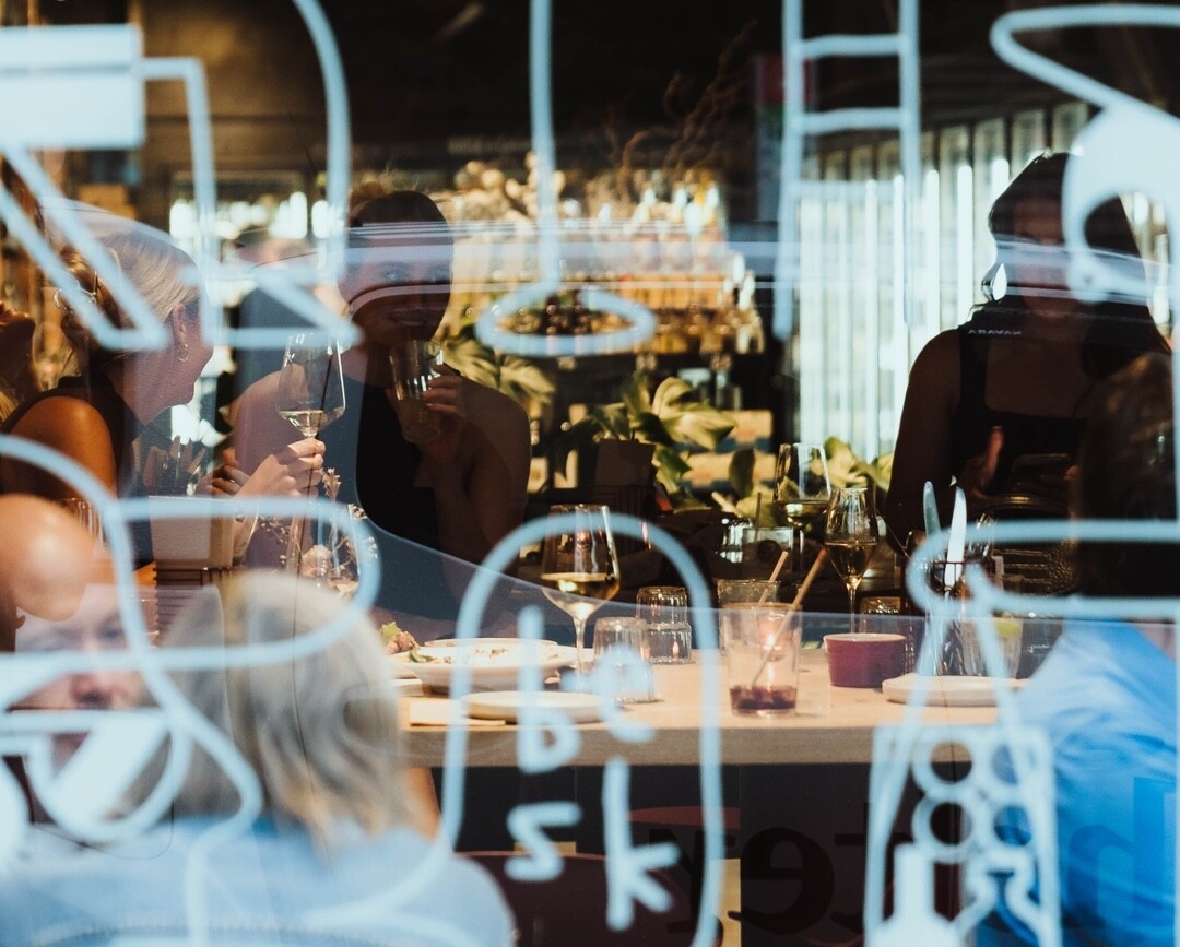 A photo through the window of Besk of people enjoy wine at a table