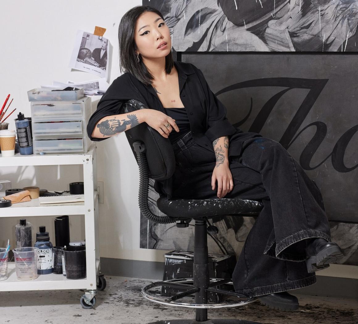 The artist Anna Park sits in front of one of her artworks