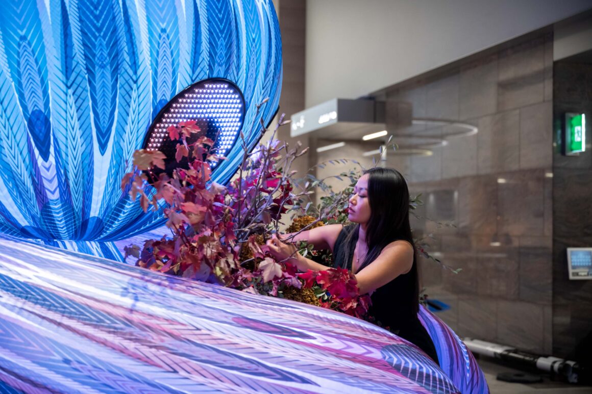 A woman placing flowers in the art installation Stem by Stem