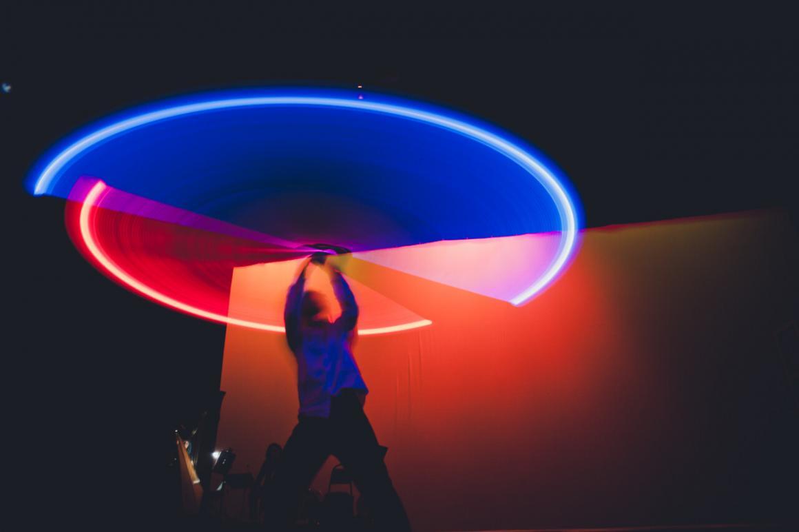 A man spinning glowing blue and red sticks above his head to create a circle
