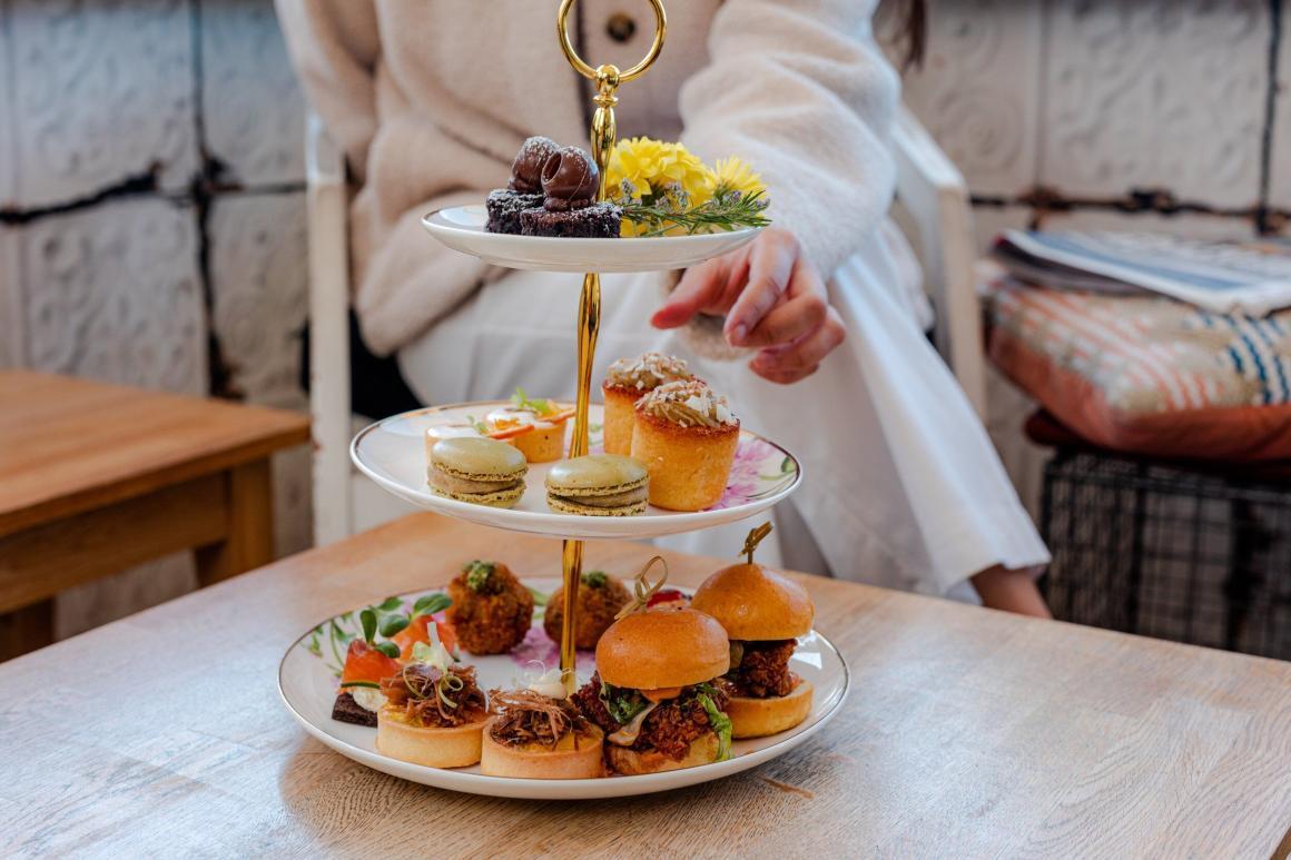 A woman reaching for a cake on a stand full of little high tea treats