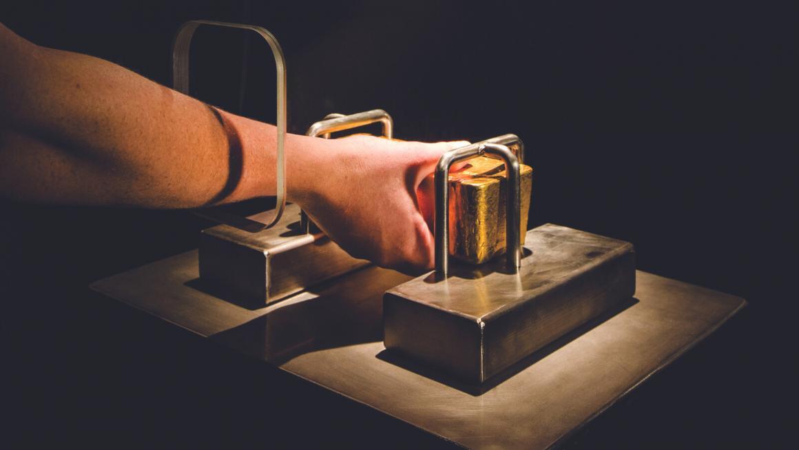 A visitor feels and holds a gold bar in a case