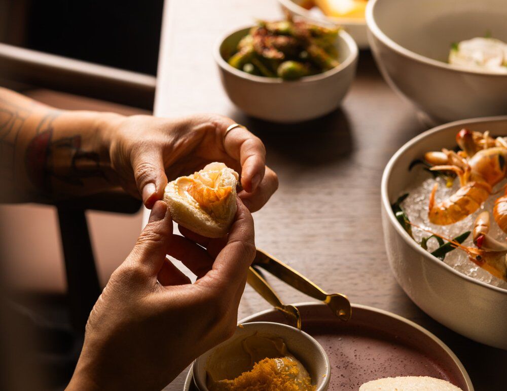 A person holding a bao bun at a table with several other asian dishes on it
