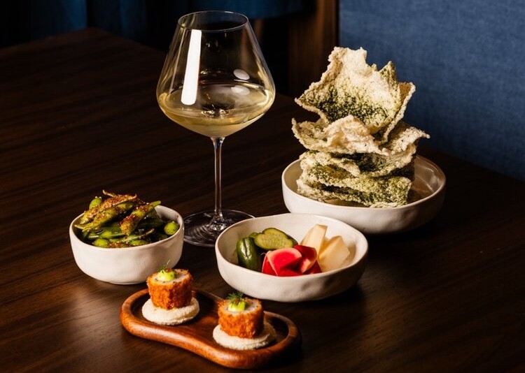 A spread of asian dishes and a wine on a wooden table at Papi Katsu