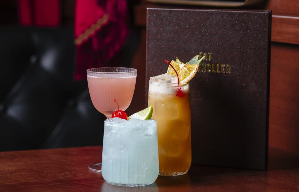 Three cocktails sitting on a table with a menu behind them at Fat Controller