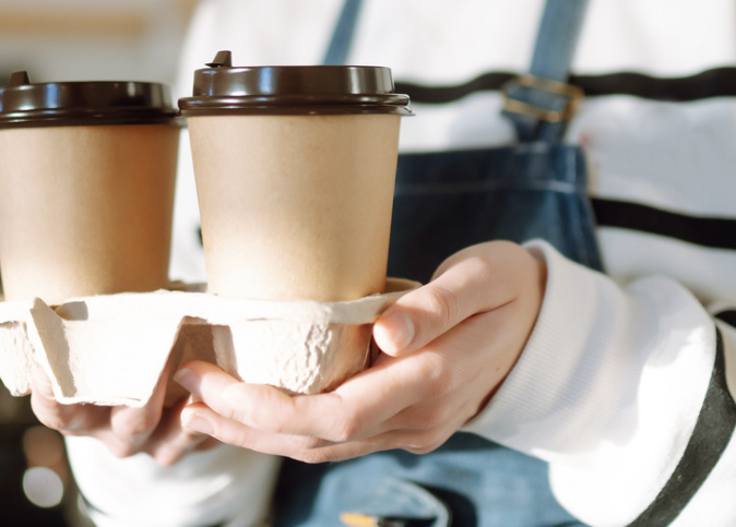 A woman holding two takeaway coffee cups at ground.