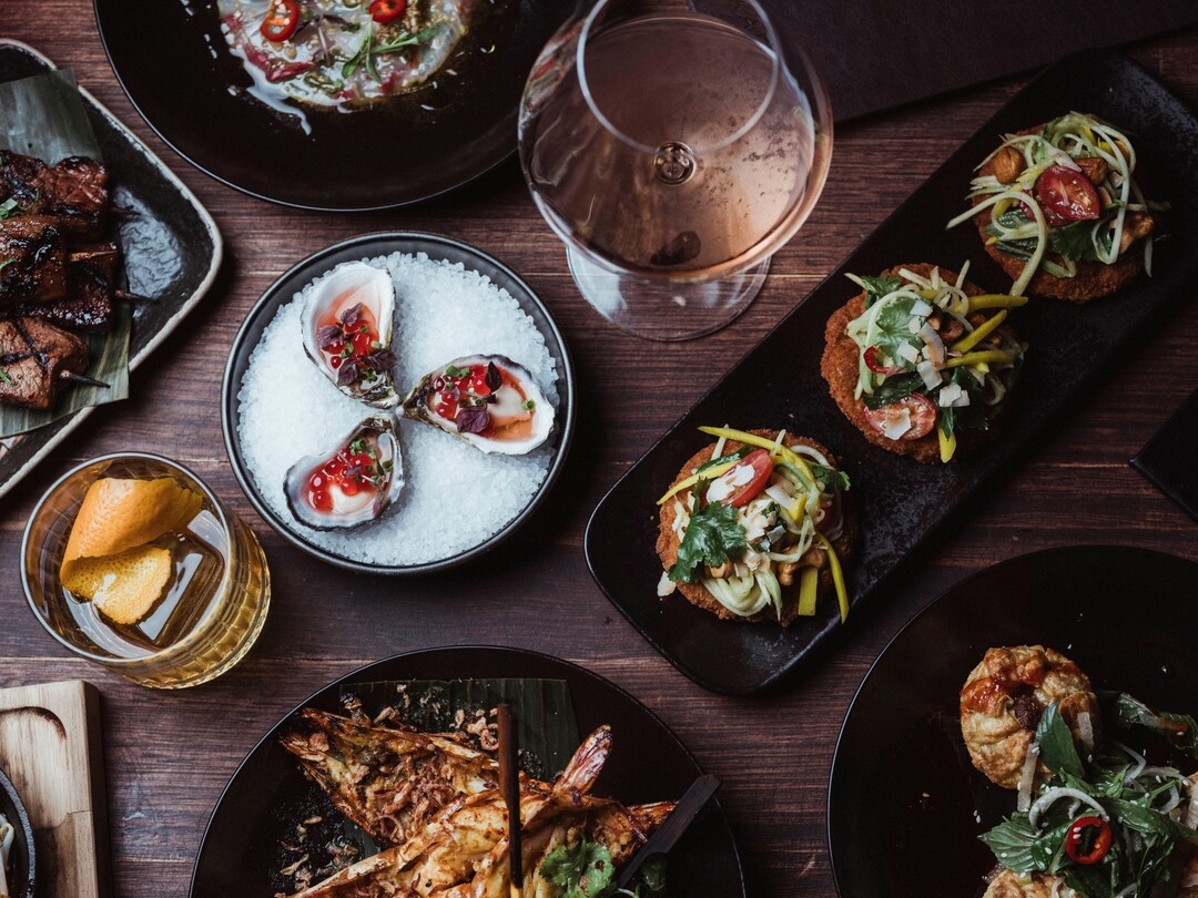 A spread of food and drinks on a table at Karla including oysters, skewers and a negroni