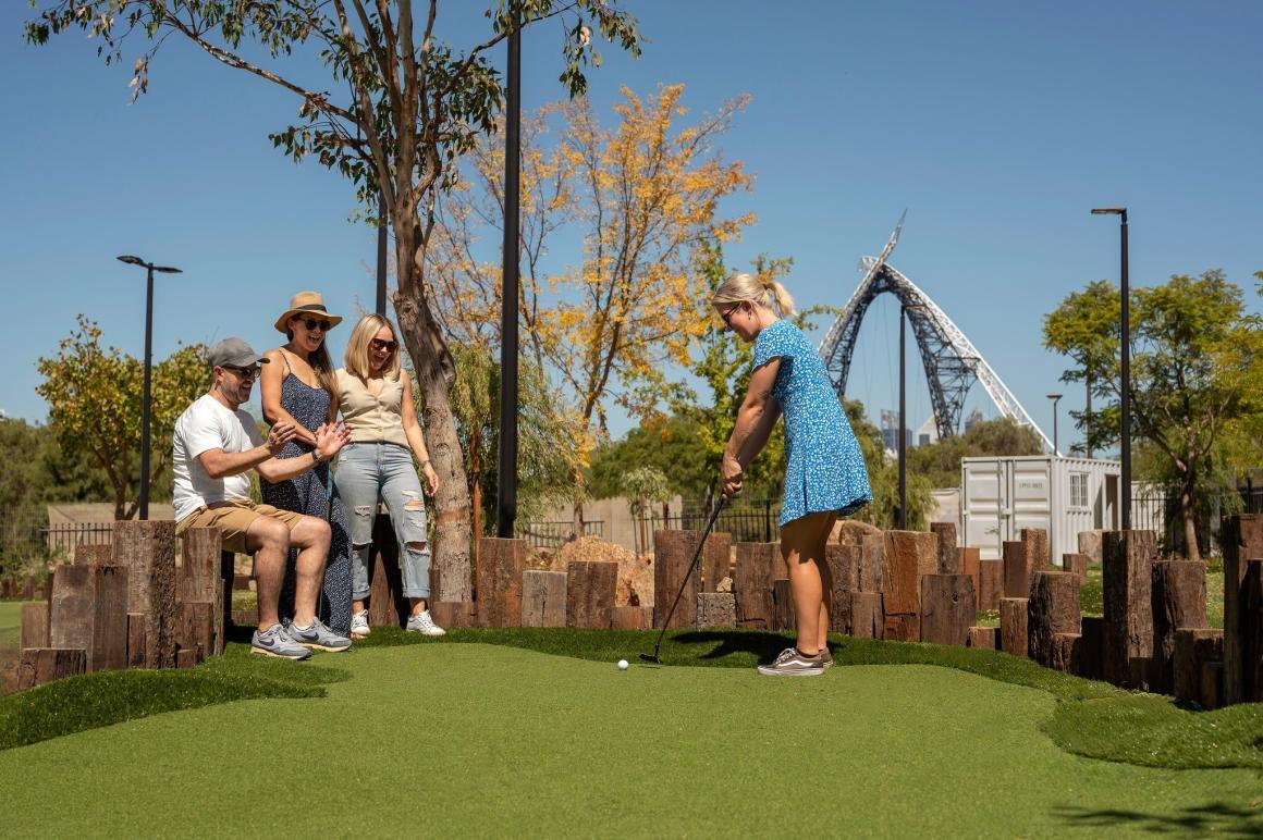 A group of friends plays mini golf at Matagarup with the iconic bridge in the background