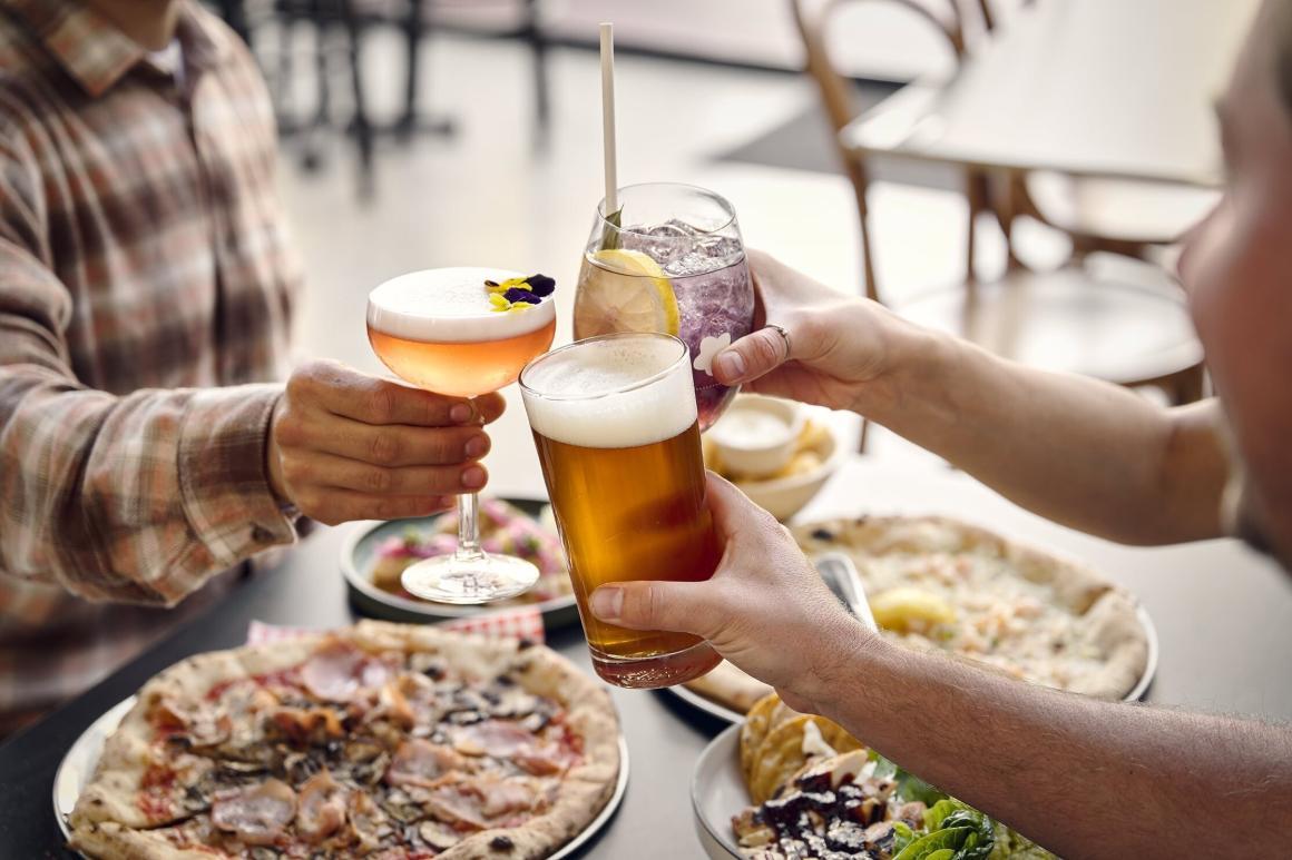 Three people cheers beers and cocktails over a table of pizzas at Southcamp in Dunsborough 