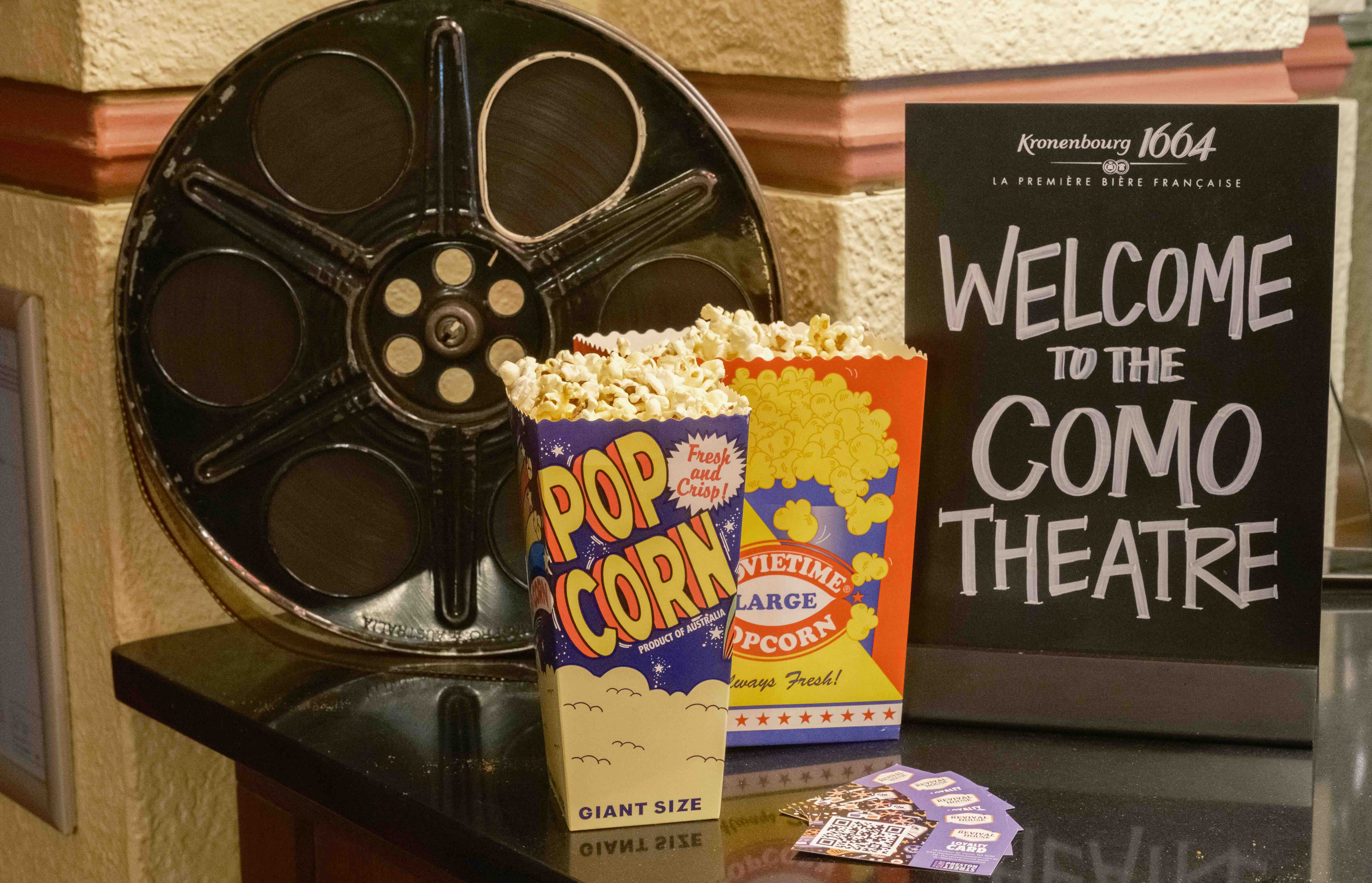 A 35mm reel, popcorn and tickets sit on a bench with a "Welcome to the Como Theatre" sign. At Exhumed cinema during Strange Festival