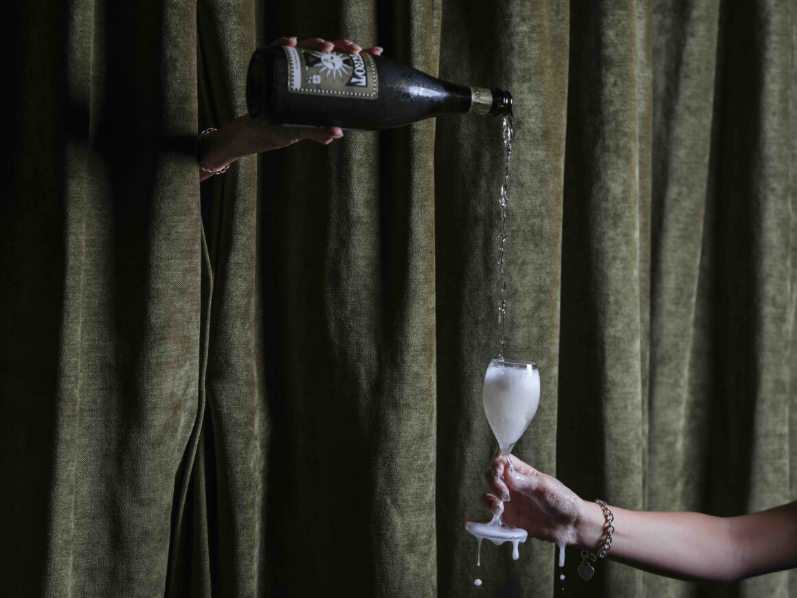 A hand coming through a green curtain pouring wine into a glass at W Churchill during Plateful Perth in Brookfield Place