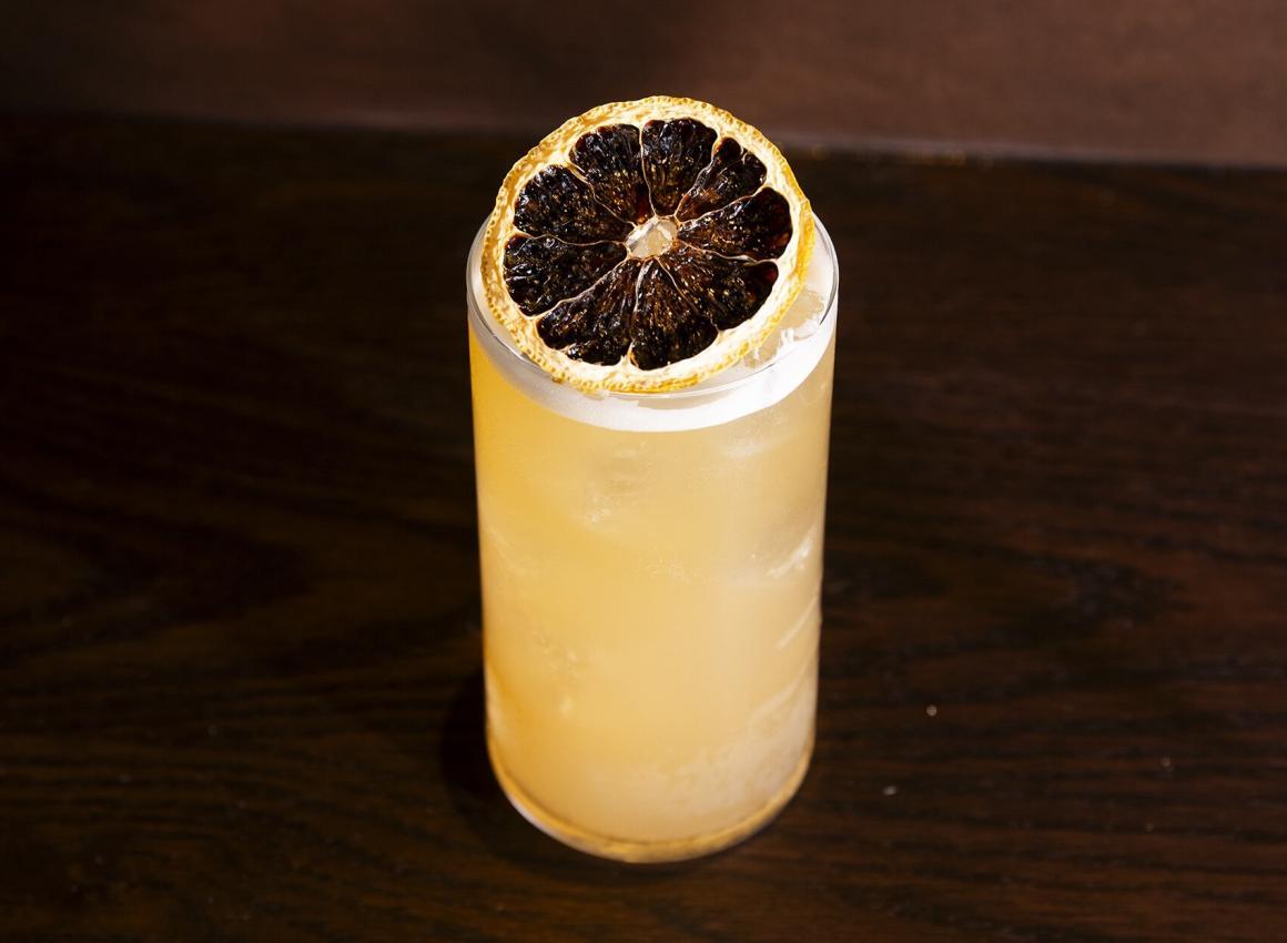 A cocktail sitting on a wooden table, adorned with a dried lemon at Cassia Restaurant in Fremantle