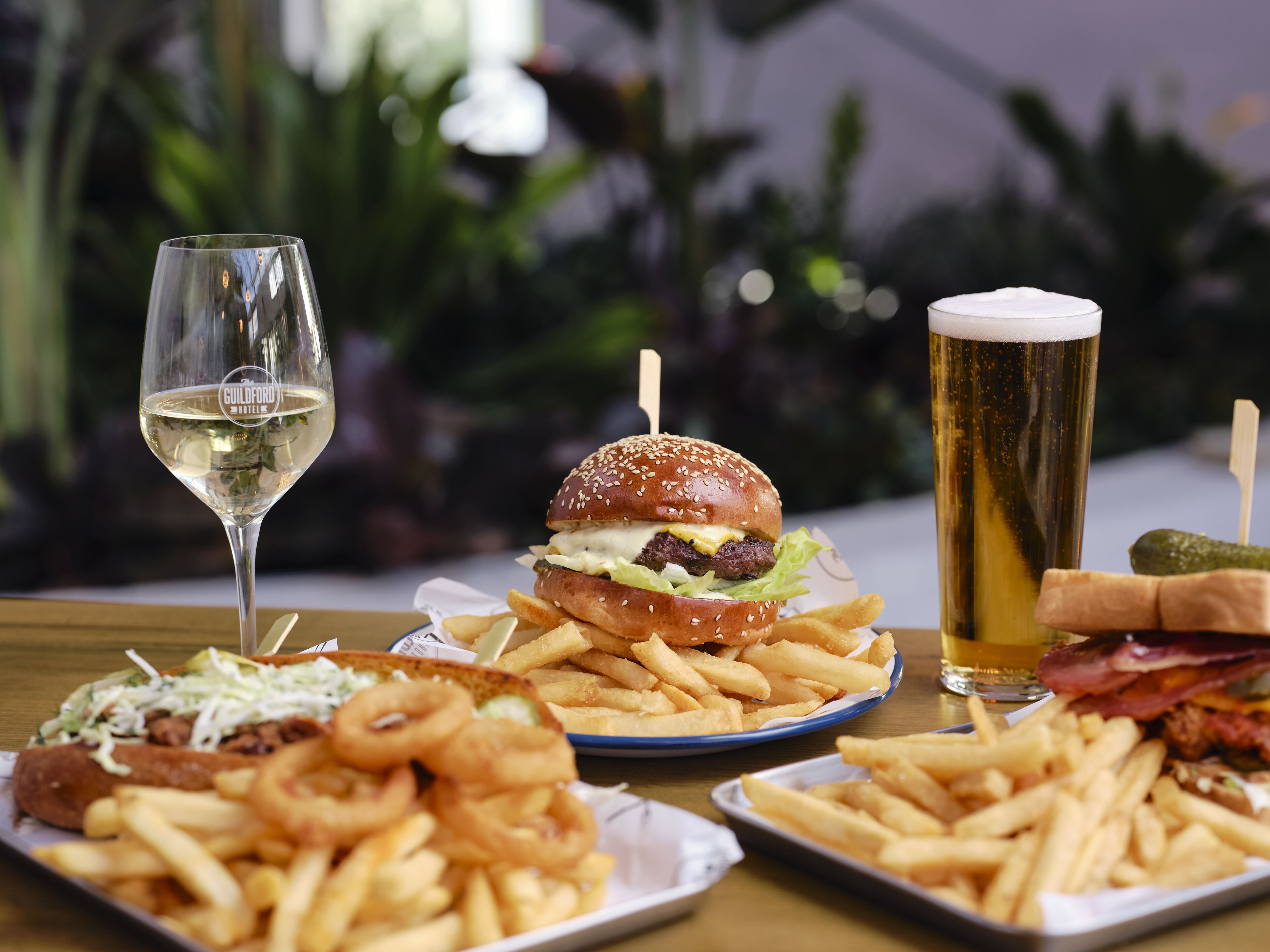 Several food dishes including burgers and fish and chips on a table with a glass of wine and pint of beer at the Vaudeville Hall at Perth's Guildford Hotel