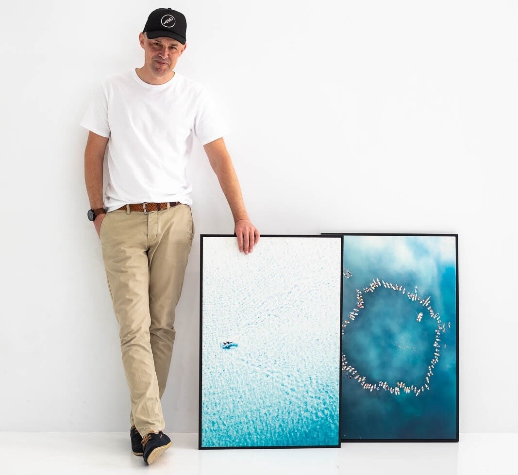 Drone photographer Nick Bennett of Tailwinds Aerial Media stands with two of his photographs