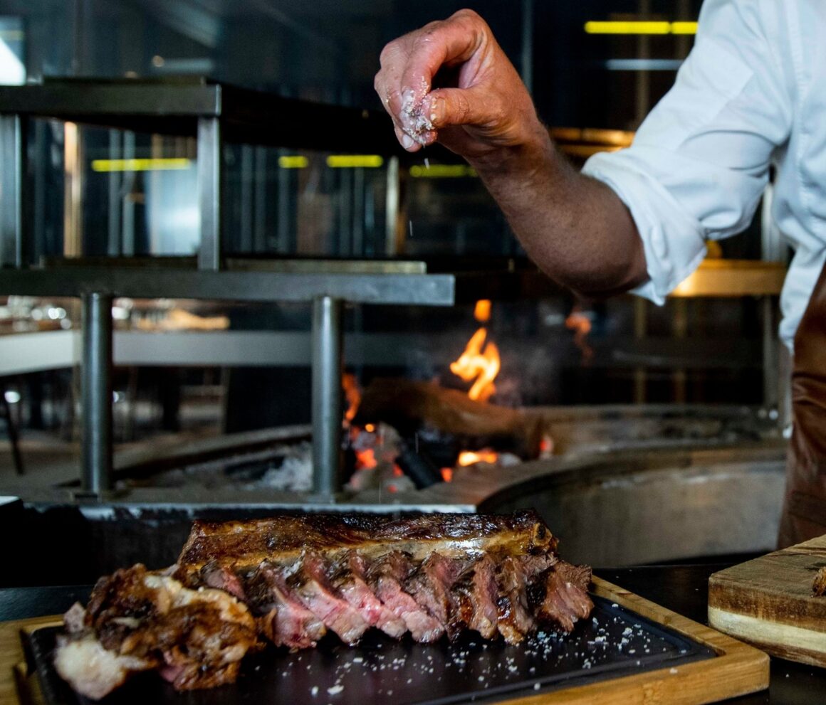 A chef putting salt on steak at Ascua, one of Perth's best steakhouses 