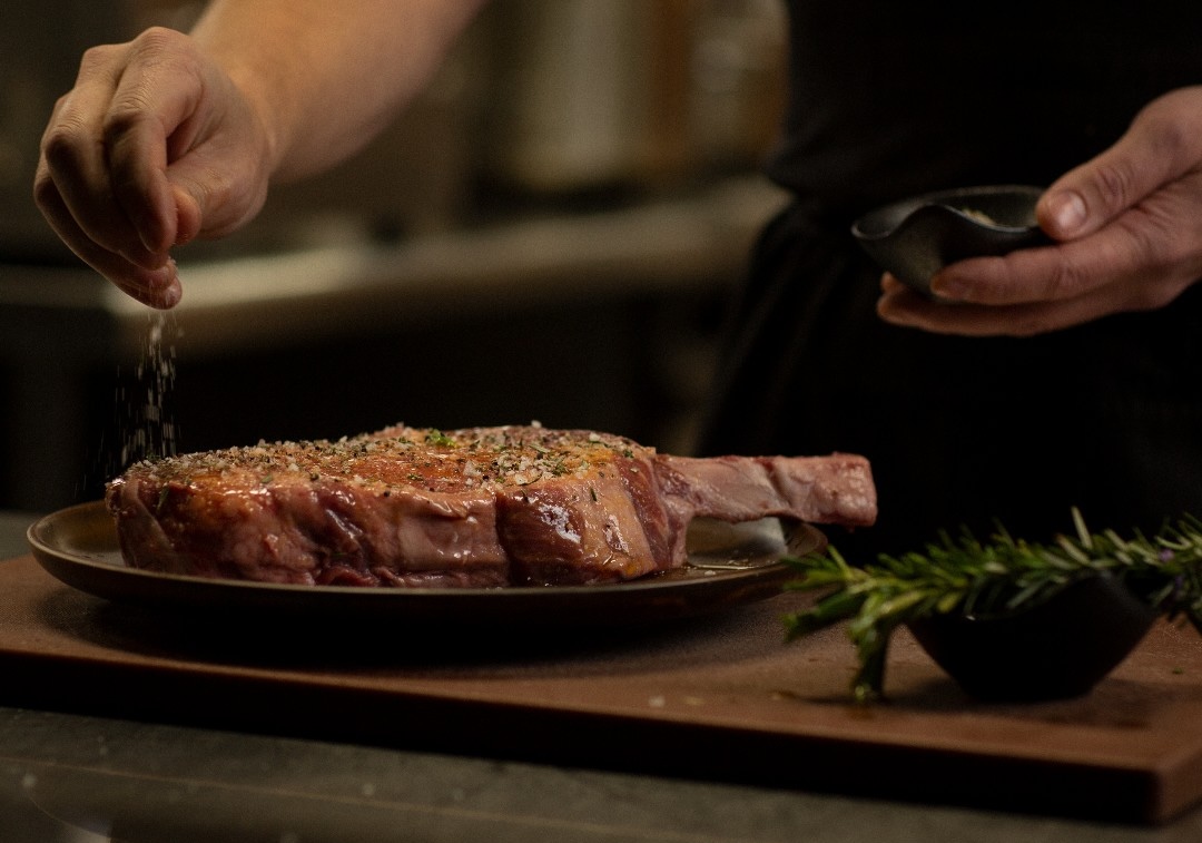A chef putting seasoning on a steak at the Steak House, one of Perth's best steakhouses 
