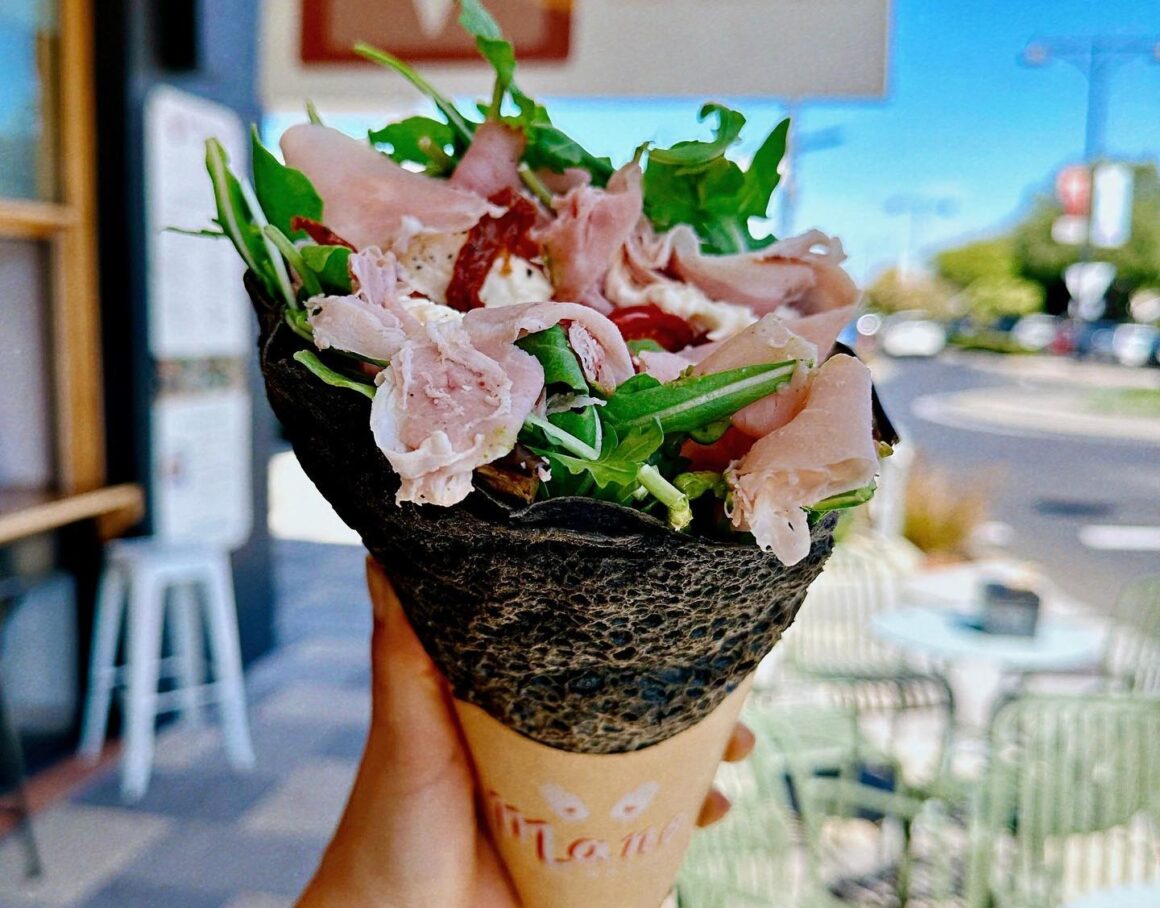 A woman holding at wrap from Mano Wraps, A spread of food on the table at INARA, one of the best food spots in Busselton
